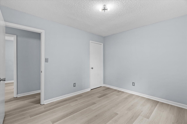 empty room featuring light wood-style floors, baseboards, and a textured ceiling