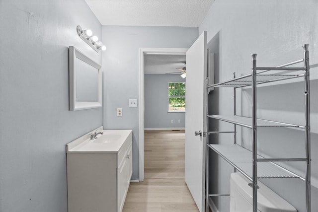 bathroom with ceiling fan, vanity, toilet, a textured ceiling, and wood finished floors