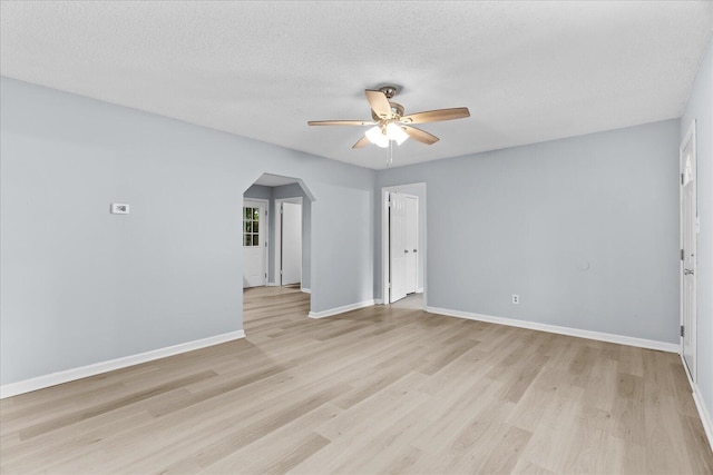 unfurnished room featuring baseboards, arched walkways, light wood finished floors, and ceiling fan