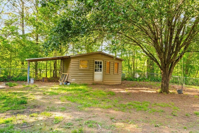 view of outbuilding with fence, a carport, and an outdoor structure