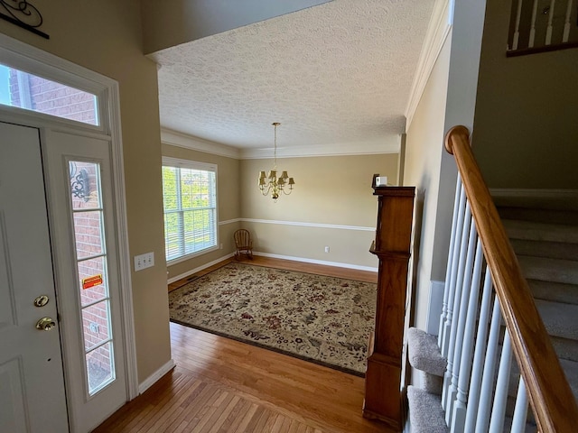 entrance foyer with a textured ceiling, crown molding, stairway, wood-type flooring, and a chandelier