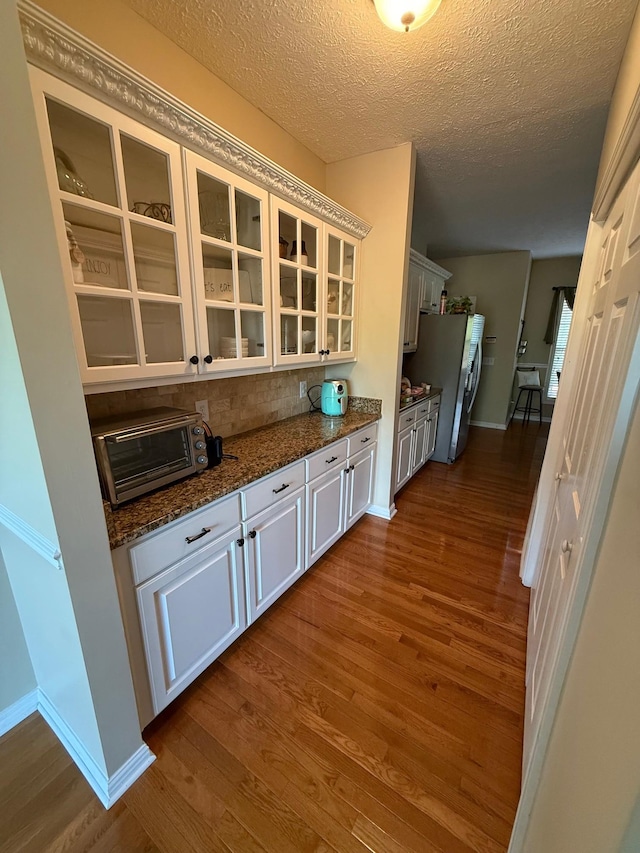 kitchen with freestanding refrigerator, a toaster, glass insert cabinets, dark wood-style floors, and dark stone countertops