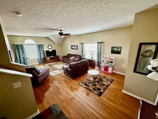 living area with wood finished floors, baseboards, a textured ceiling, a ceiling fan, and vaulted ceiling