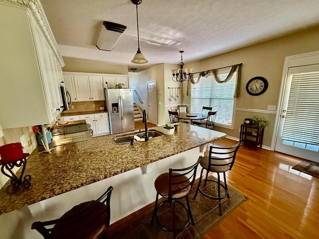 kitchen with dark wood-style flooring, a sink, a peninsula, a breakfast bar, and stainless steel appliances
