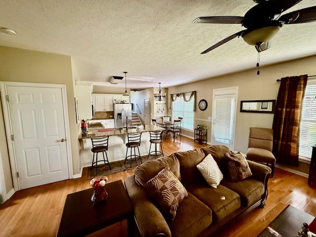 living room featuring baseboards, a ceiling fan, a textured ceiling, and wood finished floors