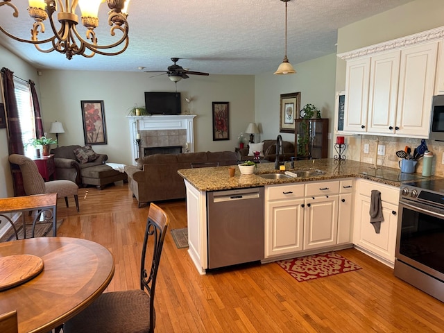 kitchen with a peninsula, ceiling fan with notable chandelier, open floor plan, a sink, and appliances with stainless steel finishes