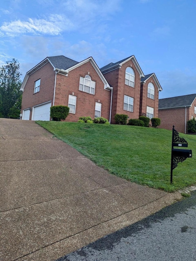 view of front of house with an attached garage, a front yard, brick siding, and aphalt driveway