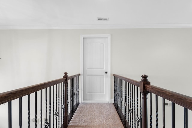 hallway featuring visible vents, ornamental molding, carpet floors, baseboards, and an upstairs landing