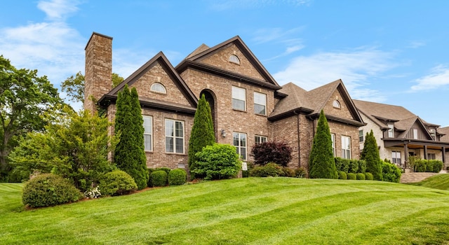 view of front facade with brick siding, a front lawn, and a chimney
