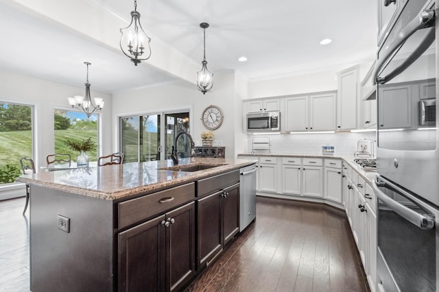 kitchen with a kitchen island with sink, dark brown cabinets, a chandelier, a sink, and stainless steel appliances