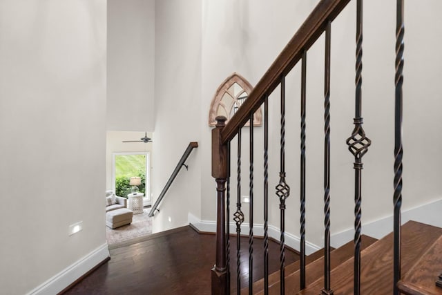 stairway featuring baseboards, a high ceiling, and wood finished floors