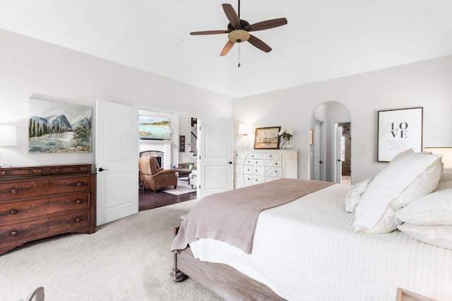 carpeted bedroom with arched walkways, high vaulted ceiling, and a ceiling fan