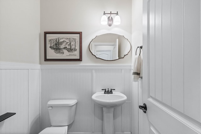 half bathroom featuring a decorative wall, toilet, a sink, and a wainscoted wall