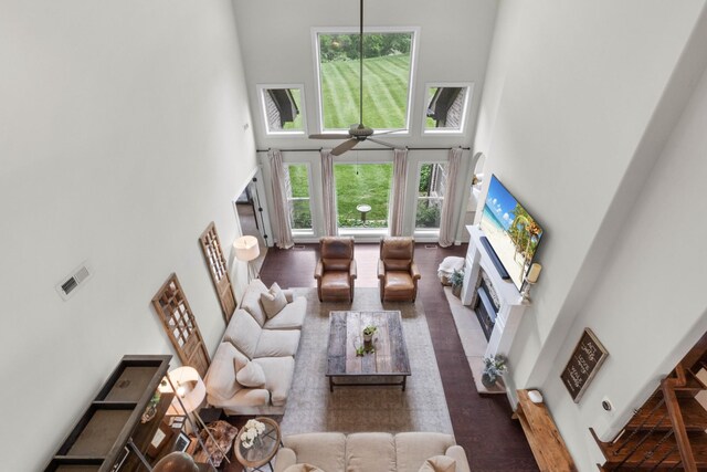 living room featuring a fireplace with flush hearth, a high ceiling, ceiling fan, and visible vents