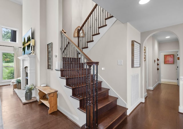 staircase with arched walkways, baseboards, wood finished floors, and a towering ceiling