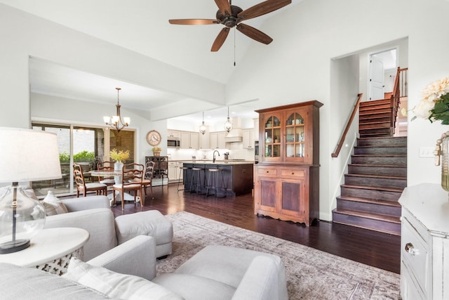 living room featuring dark wood-type flooring, ceiling fan with notable chandelier, and stairway