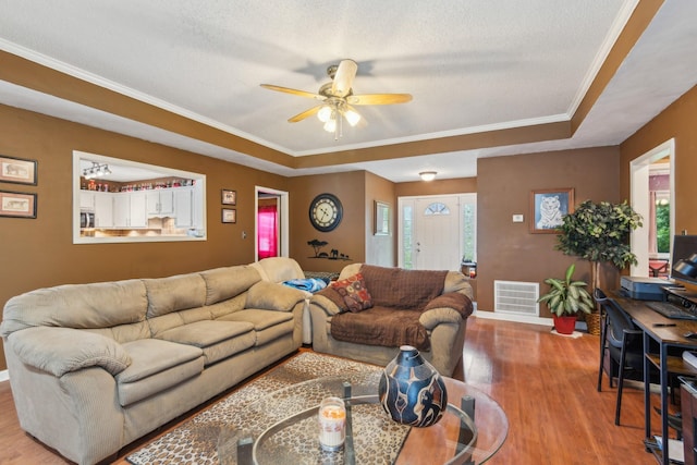 living area featuring ceiling fan, a raised ceiling, baseboards, wood finished floors, and visible vents