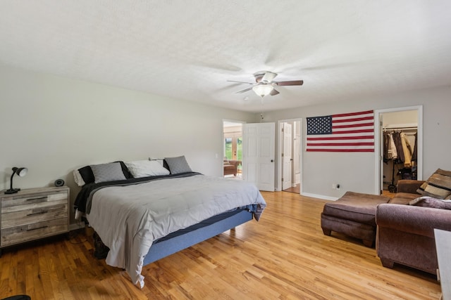 bedroom featuring ceiling fan, baseboards, a closet, a spacious closet, and light wood-style flooring