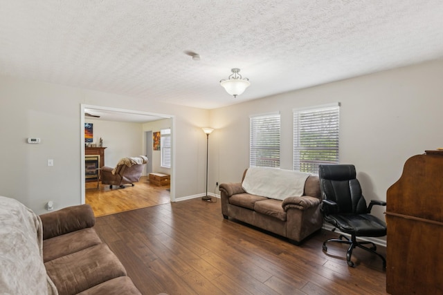 living room with baseboards, a textured ceiling, a glass covered fireplace, and hardwood / wood-style floors