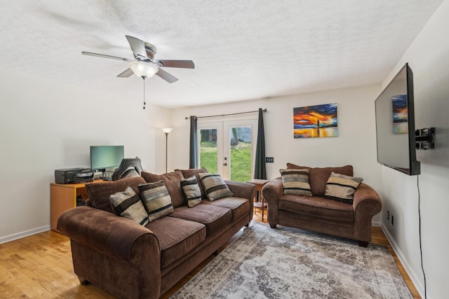 living room featuring ceiling fan, a textured ceiling, french doors, baseboards, and wood finished floors