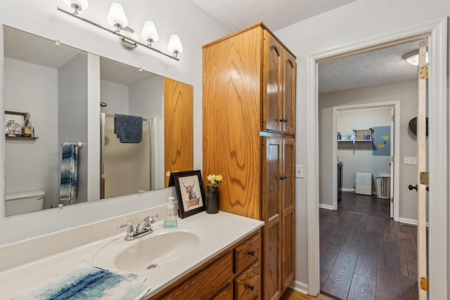 bathroom with vanity, wood finished floors, a shower, toilet, and baseboards
