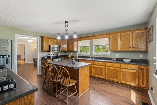 kitchen featuring a kitchen island, dark countertops, brown cabinets, a sink, and appliances with stainless steel finishes