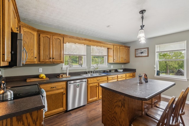 kitchen featuring appliances with stainless steel finishes, dark countertops, a sink, dark wood-style floors, and a breakfast bar