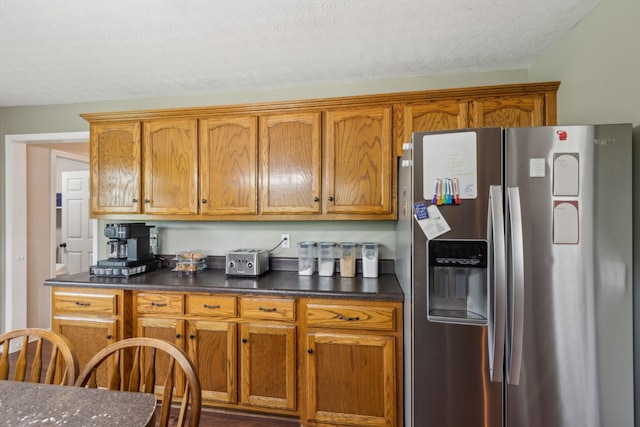 kitchen with dark countertops, brown cabinetry, stainless steel refrigerator with ice dispenser, and a textured ceiling