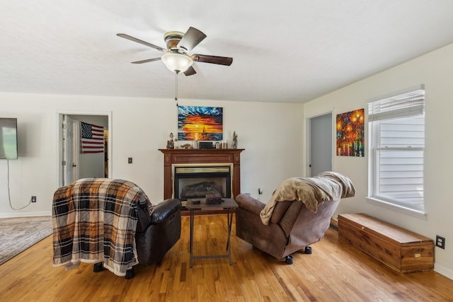 living room featuring a ceiling fan, baseboards, wood finished floors, and a fireplace