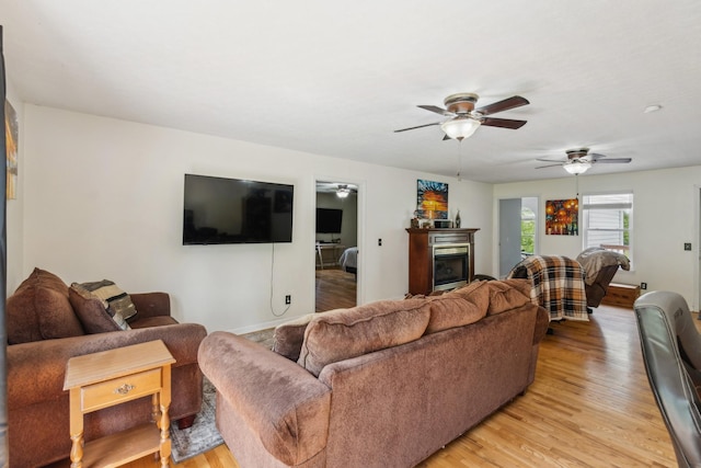 living area with a ceiling fan, baseboards, a glass covered fireplace, and light wood finished floors