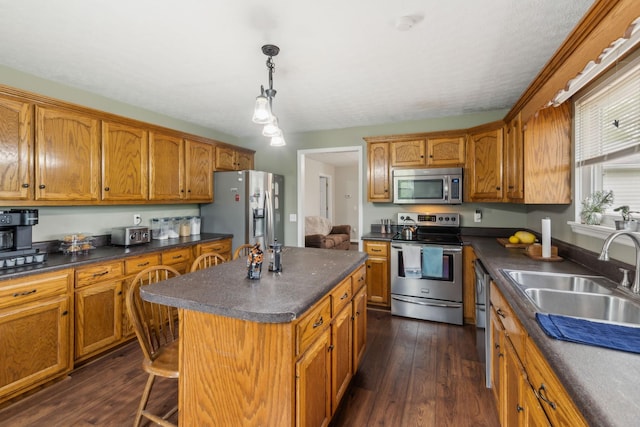 kitchen featuring brown cabinetry, a sink, appliances with stainless steel finishes, and dark countertops