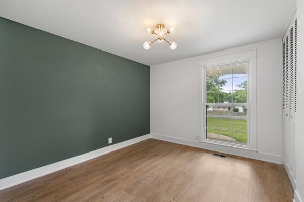 unfurnished room featuring an inviting chandelier, baseboards, wood finished floors, and visible vents