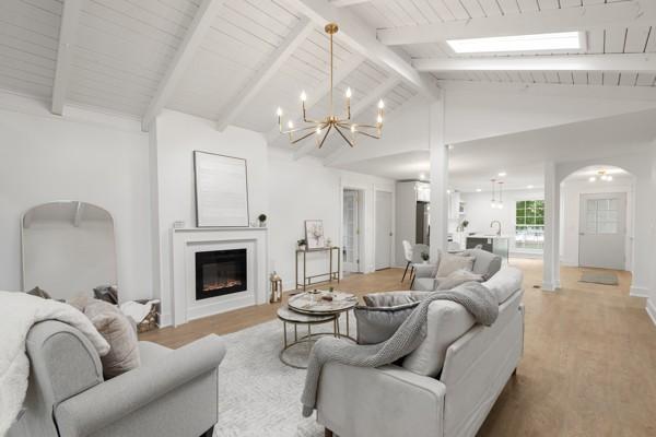 living area featuring arched walkways, a fireplace, light wood-type flooring, and a notable chandelier