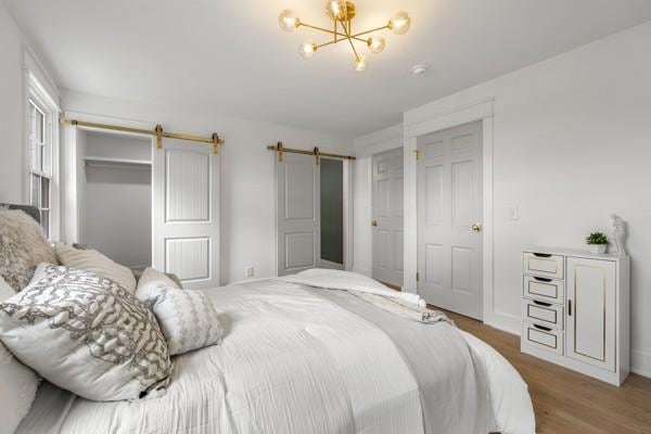 bedroom featuring baseboards, a chandelier, a barn door, and wood finished floors