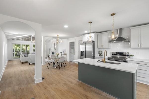 kitchen with appliances with stainless steel finishes, a sink, light countertops, light wood-style flooring, and wall chimney exhaust hood