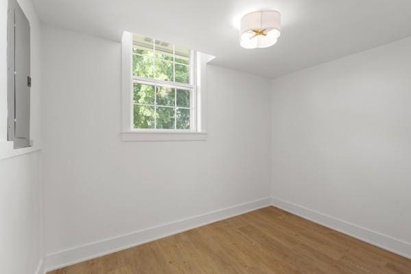 spare room with baseboards, electric panel, and light wood-type flooring