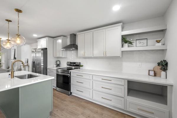 kitchen with light countertops, wall chimney exhaust hood, a sink, decorative light fixtures, and stainless steel appliances