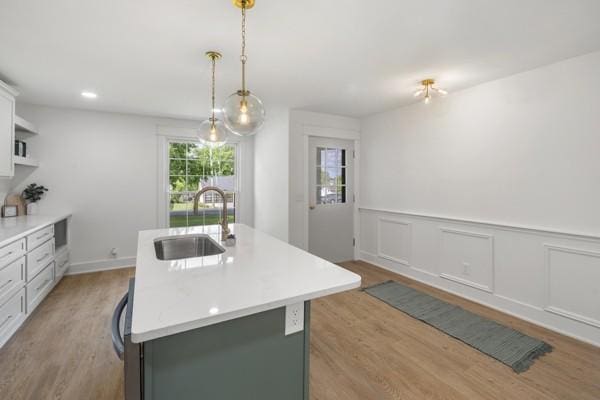 kitchen with light wood-type flooring, a sink, a center island with sink, and light countertops