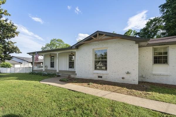 view of front facade featuring covered porch, brick siding, fence, and a front yard