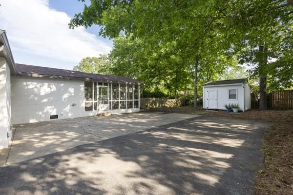 view of patio / terrace featuring fence, a storage unit, an outbuilding, and a sunroom