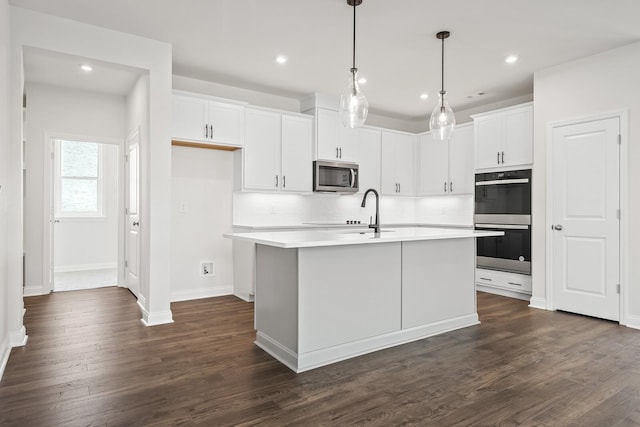 kitchen featuring light countertops, stainless steel appliances, white cabinetry, dark wood-type flooring, and a center island with sink