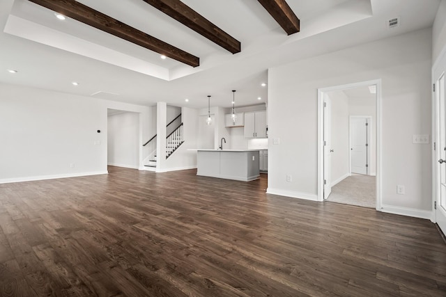 unfurnished living room with visible vents, dark wood finished floors, and beam ceiling