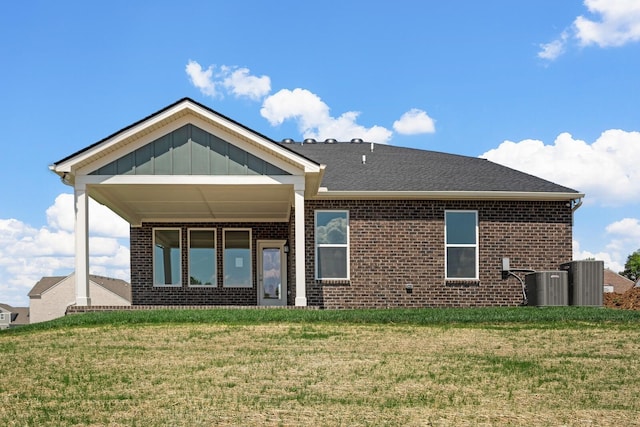 back of property featuring a yard, brick siding, board and batten siding, and central AC unit