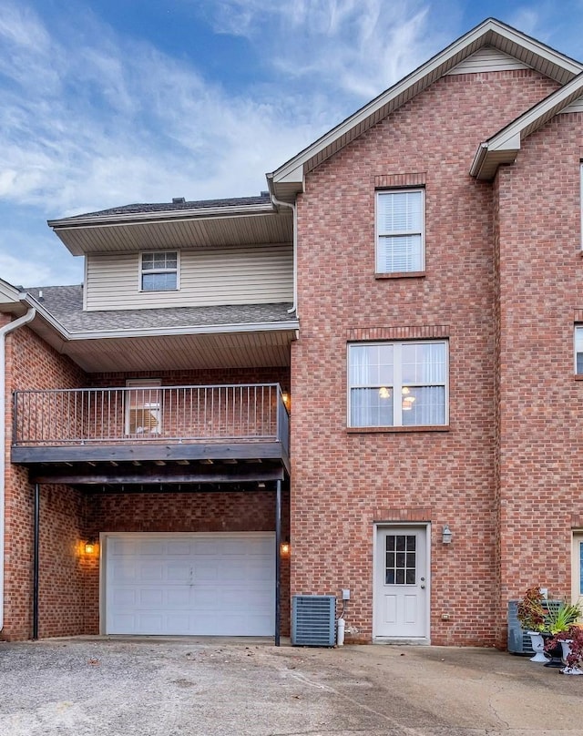 view of front facade featuring brick siding, a garage, central AC unit, a balcony, and driveway
