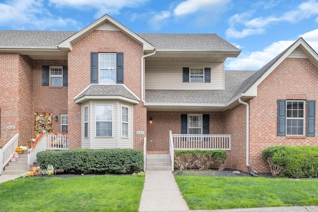 traditional home featuring covered porch, a shingled roof, brick siding, and a front yard