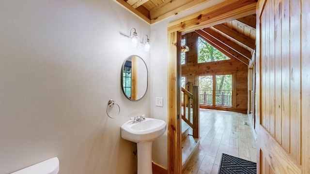 bathroom with a sink, toilet, wooden walls, vaulted ceiling with beams, and hardwood / wood-style floors
