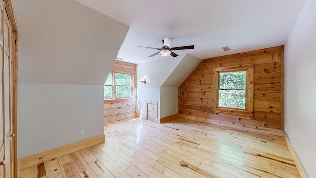 additional living space with wood walls, a ceiling fan, baseboards, light wood-type flooring, and vaulted ceiling