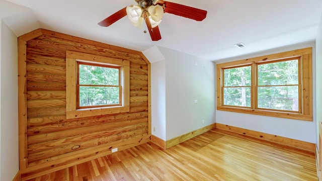additional living space featuring ceiling fan, visible vents, baseboards, rustic walls, and light wood-style flooring