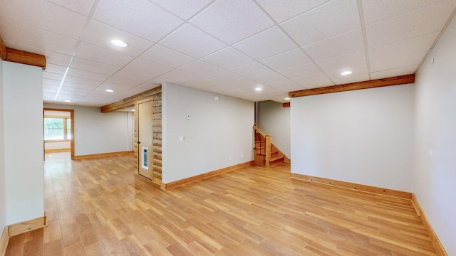 below grade area featuring baseboards, stairs, light wood finished floors, and a drop ceiling