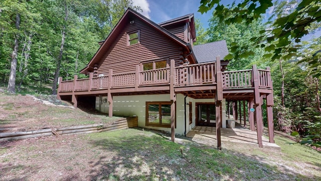 rear view of property featuring a deck, log exterior, a patio, and roof with shingles